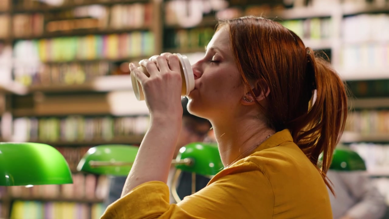 Young adult drinking coffee and typing on laptop in university library