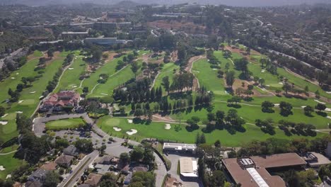 aerial drone view of golfing grounds with trees and lush green grass pathways besides the highway