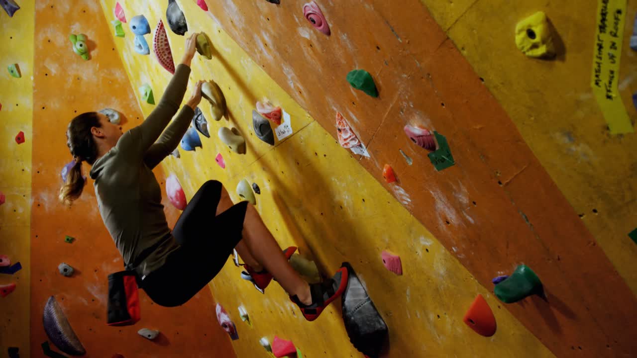 mujer escalando la pared artificial en el gimnasio de bouldering 4k