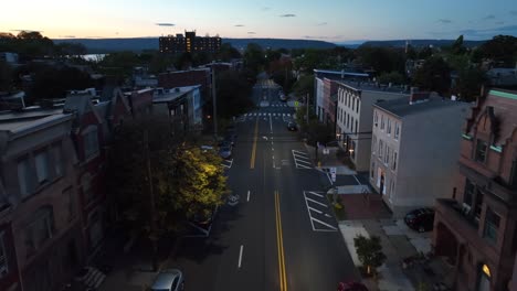 dusk over city street lined with brick townhouses and rowhomes, distant river view