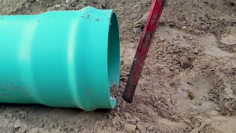 A-construction-worker-drives-a-spike-into-the-ground-in-preparation-for-assembling-gravity-sewer-pipe-on-a-construction-site