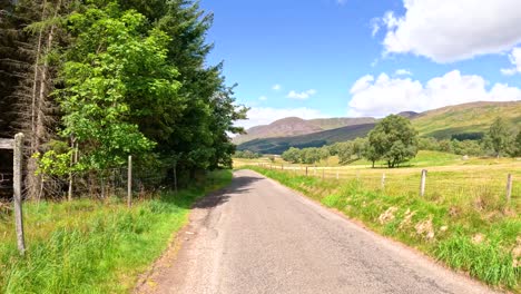 car drives along narrow rural road through green hills, trees, and farmland in clova, scotland