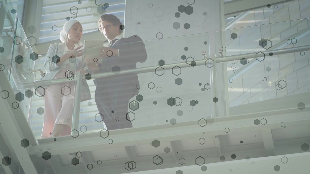 Woman presenting tablet, man pointing, both reviewing business data under shifting hex overlay