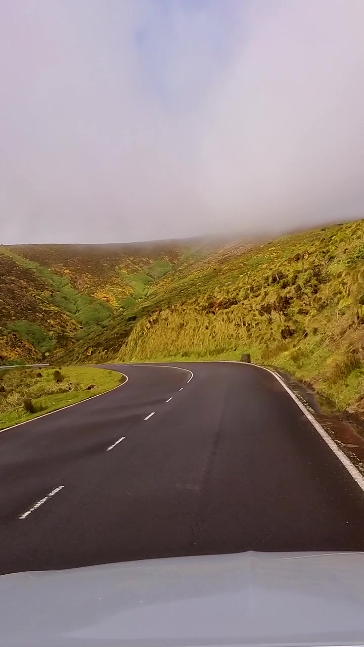 Panoramica verticale dalla prospettiva di un'auto lungo una strada di montagna tortuosa che scompare nella nebbia sull'isola di Flores, Azzorre, Portogallo