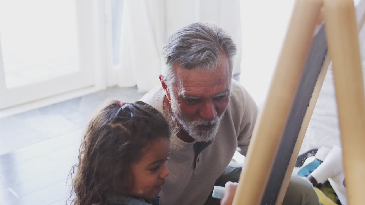 바닥에 앉아서 손녀와 함께 블랙보드에 그림을 그리는 노인