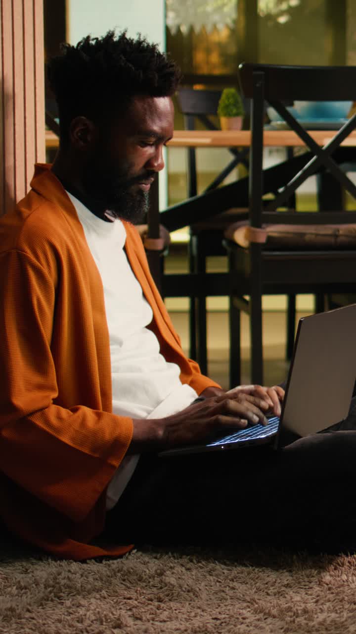 Vertical Video Cozy lifestyle scene of African American man relaxing indoors with his laptop