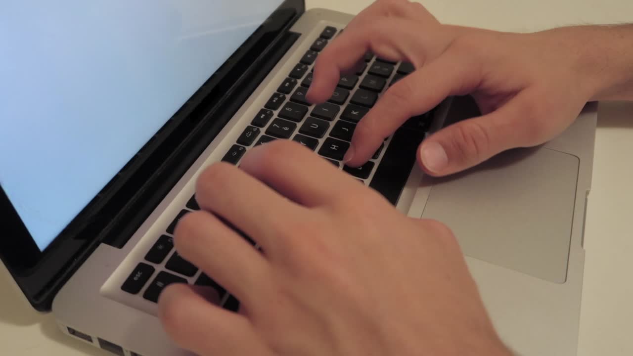 manos masculinas escribiendo en el teclado de la computadora portátil con pantalla blanca en blanco, primer plano medio