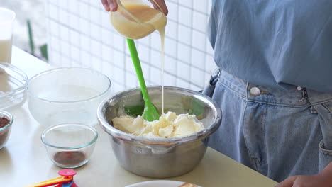 mujer vertiendo leche líquida dulce en crema batida para hacer pastel de tiramisu en casa