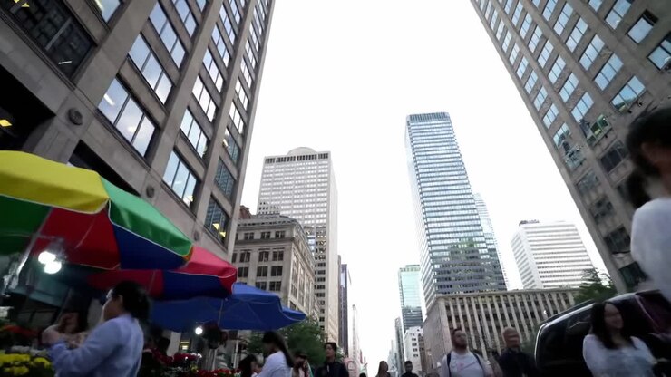 Una vivace scena urbana: persone che camminano tra grattacieli e bancarelle colorate del mercato in un vibrante paesaggio cittadino.