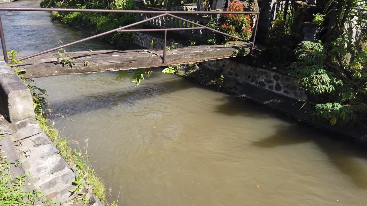 establecimiento del río de agua sucia marrón tiro, temporada de lluvias, bali indonesia luz del día puente de madera solitario