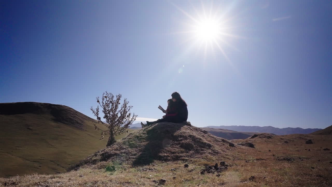 Mother reading book with daughter outdoors under bright sun during holiday trip