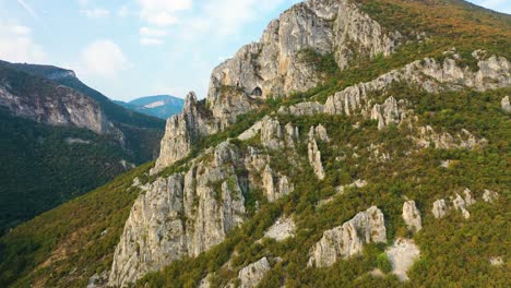 aerial zoom out cave, rocky mountain with autumn forest trees on slope