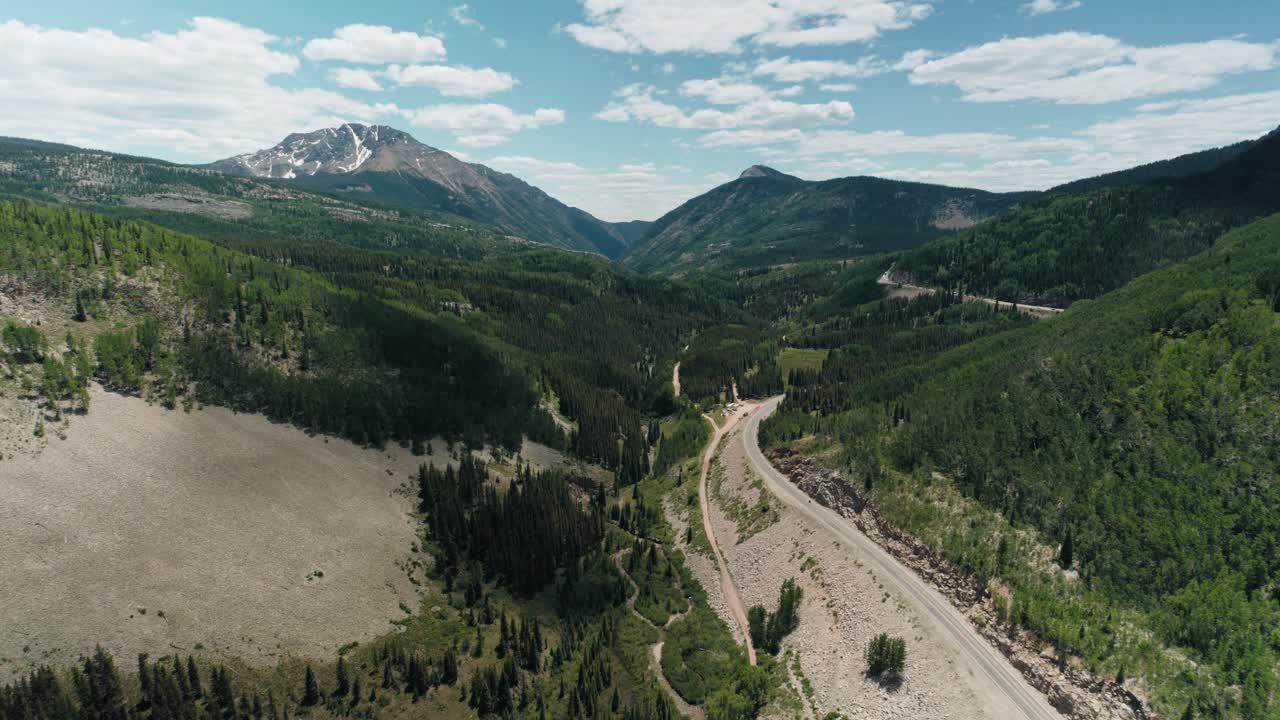 Aerial reveal of the San Juan mountain range with a road leading to the mountains.