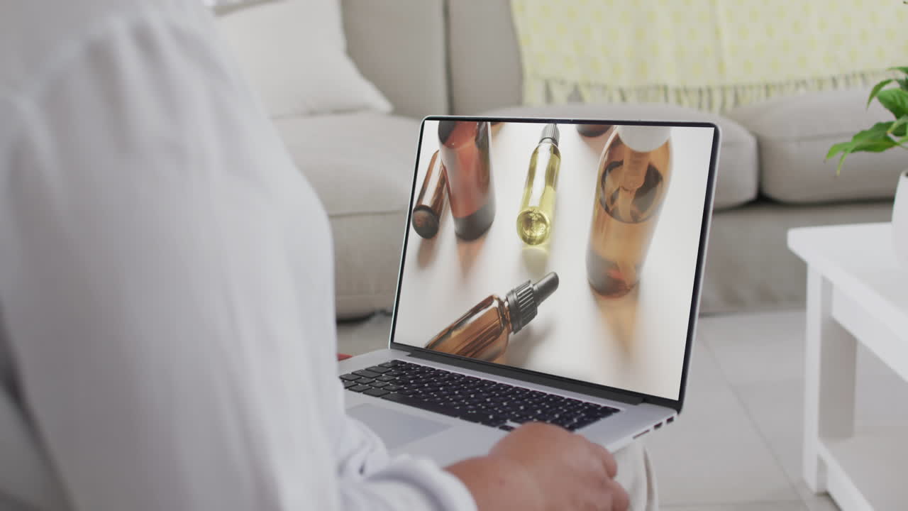 Donna di etnia mista che usa il laptop a casa per acquisti online di prodotti di bellezza, al rallentatore