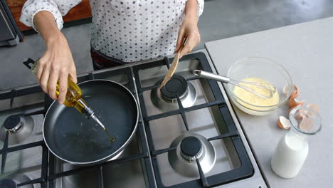 mujer biracial cocinando y vertiendo aceite en la sartén en la cocina, cámara lenta