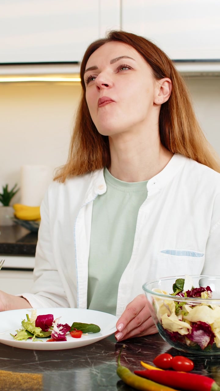 Mittelalte Frau genießt frischen Gemüsesalat in der Küche für gesunde Ernährung und Gewichtsverlust zu Hause.