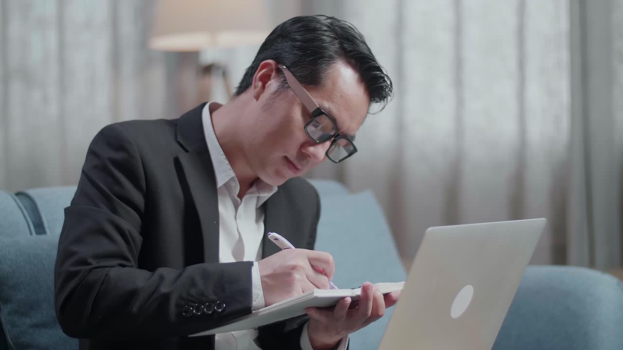 집에서 노트북으로 일하면서 노트북에 글을 쓰는 재과 쇼트를 입은 아시아 사업가의 클로즈업