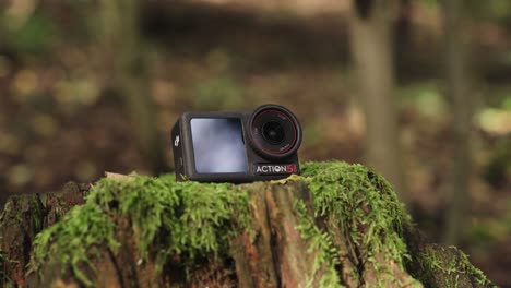 black action camera on tree stump with green moss in forest, czechia