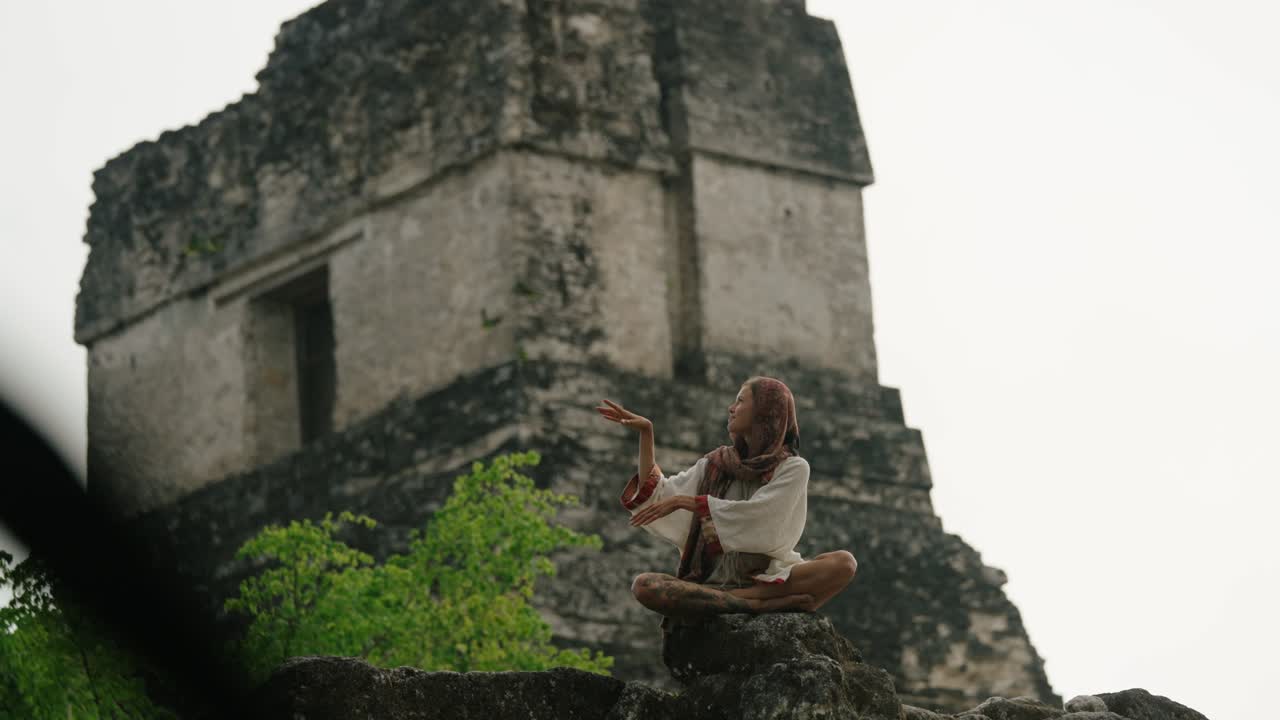 A woman practices meditation in front of an ancient Mayan pyramid at the archaeological site of Tikal, located in Petén, Guatemala.