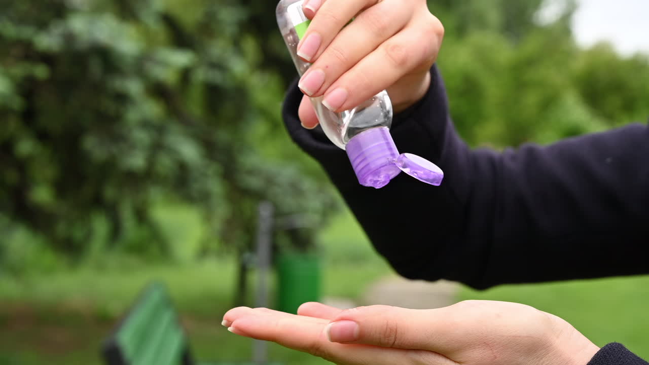 Close up of hands pouring clear sanitizer gel from a small bottle in a park
