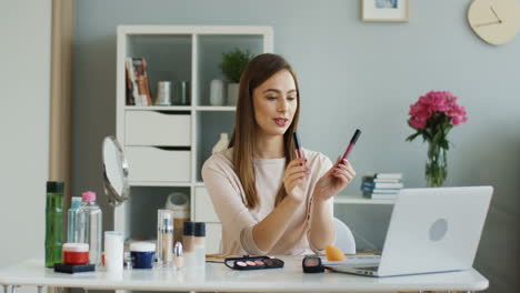 pretty beauty blogger talking about lip glosses in front of the laptop camera at home