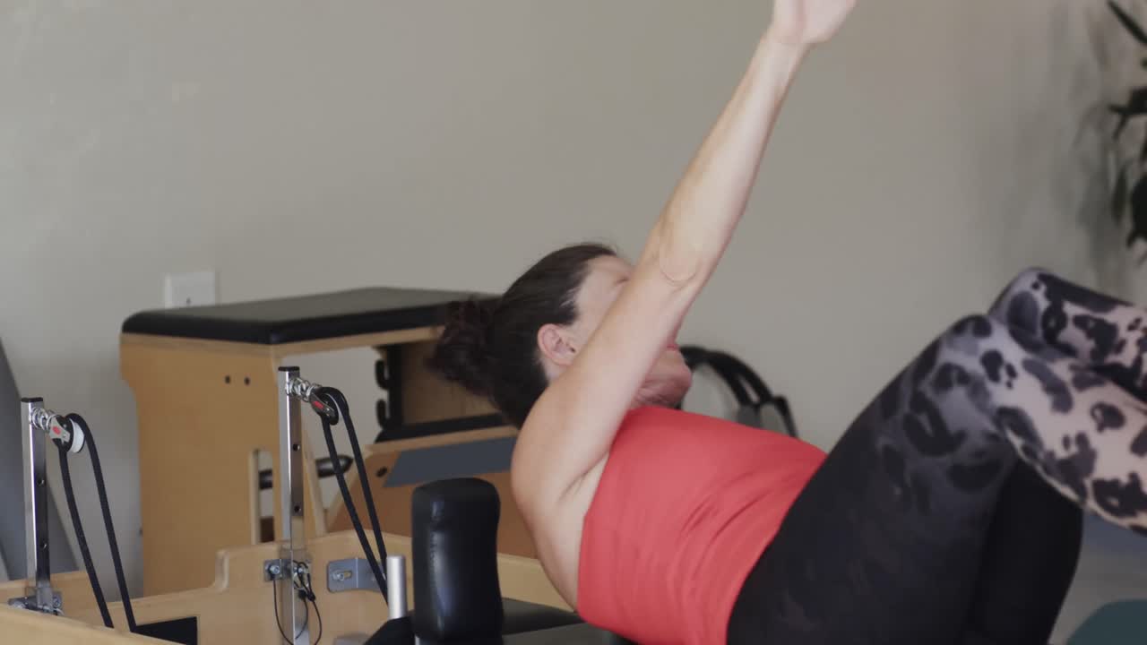 Mulher sênior caucasiana em forma alongando-se no reformer em estúdio de pilates, inalterado, em câmera lenta