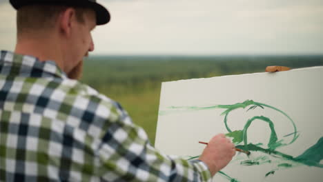 a painter, dressed in a checkered shirt, is seen gently applying green paint to a large white canvas in an outdoor setting. focusing on the delicate strokes of green on the canvas