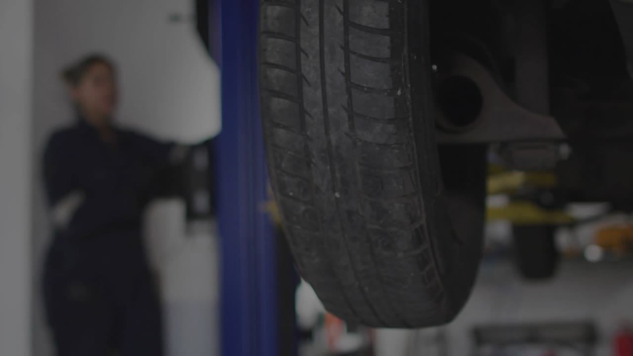 Female mechanic inspecting raised tire on shop lift starting overlay scanning codes with red lasers