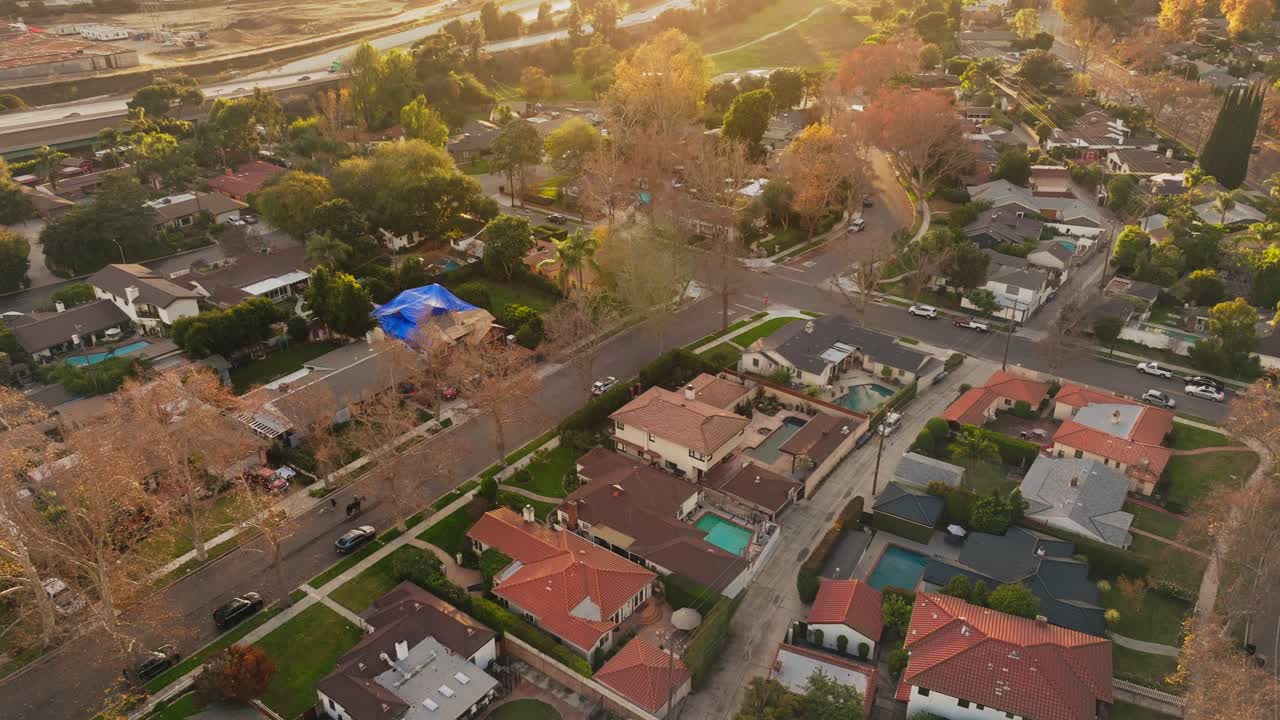 imágenes aéreas de un barrio lujoso en california al atardecer, estableciendo una toma de grandes casas con piscinas y hermosos patios vistos desde un avión no tripulado por encima, coches en la autopista en el fondo
