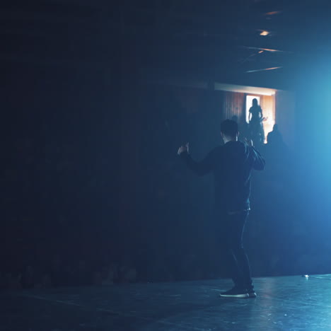modern dance class or performance in blur dark auditorium. bearded man in black sport clothes entertaints the audience with his hip-hop dance.