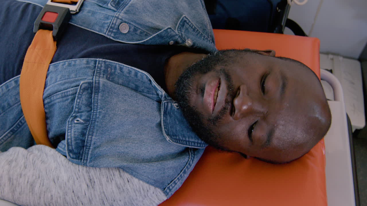 vista superior de un paramédico hablando con un paciente acostado en la camilla dentro de una ambulancia mientras toca su mano