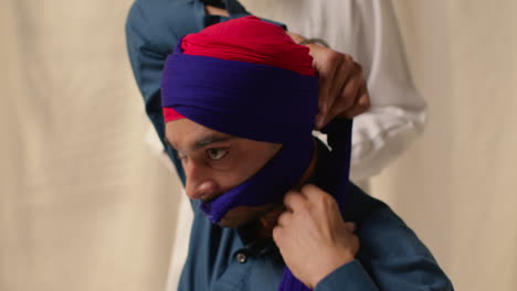 fotografía de estudio de cerca de dos hombres sikh atando tela para el turbante contra un fondo plano