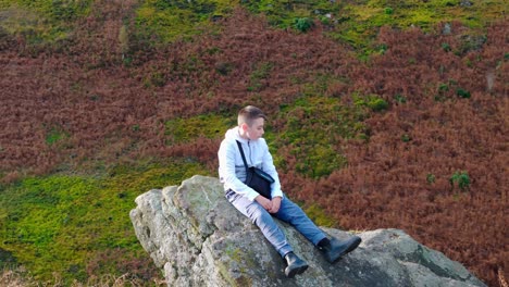 un niño se sienta en un gran afloramiento de roca, contemplando los alrededores del páramo