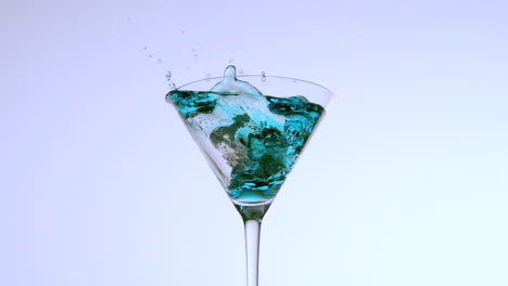 Ice-falling-into-cocktail-glass-of-blue-liquid-on-white-background