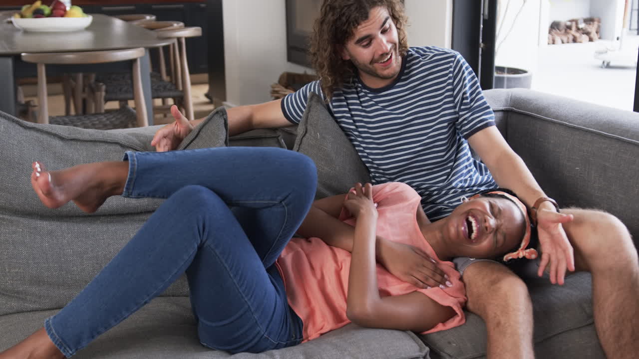 una pareja diversa, una joven afroamericana y un hombre caucásico, disfrutan de un momento lúdico en casa.