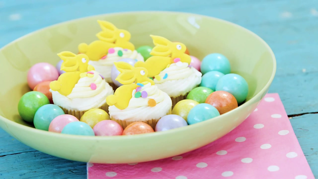 Mint bowl holding cupcakes and eggs, gold confetti falling, lens shifting closer showing treats