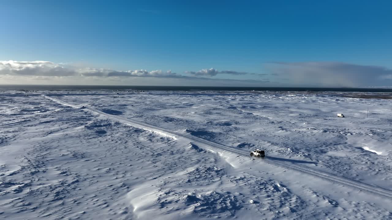 Aerial view of a lone 4x4 crossing the frozen Reykjanes Peninsula near Kleifarvatn, with endless snowfields, low winter light, and remote Icelandic wilderness