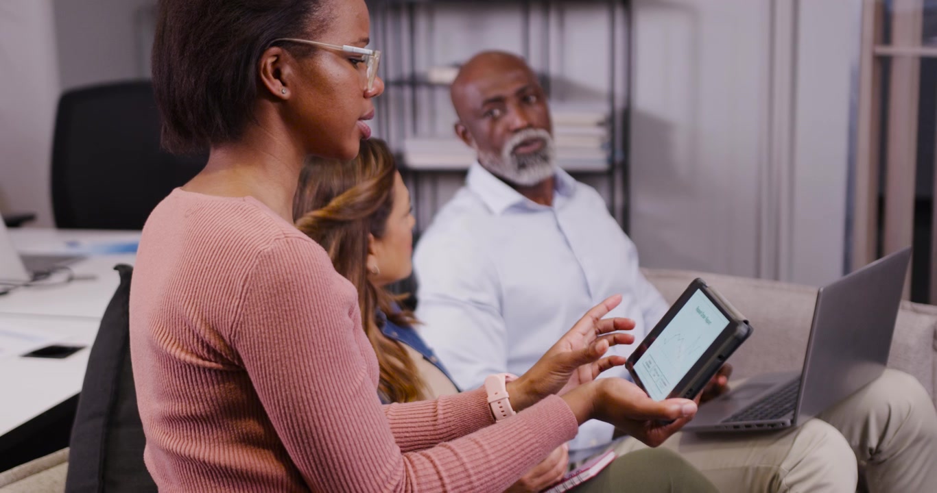 Diverse team starting meeting in office, presenter tapping tablet, peers using laptop, copy space