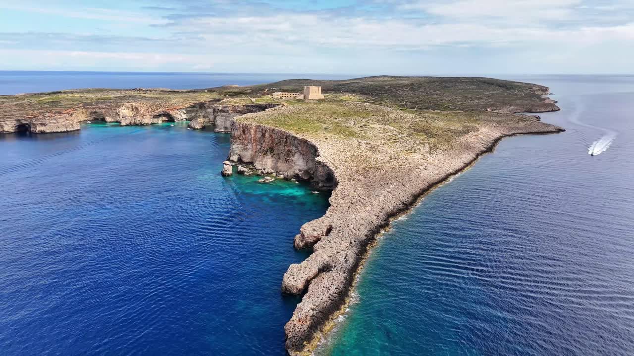 マルタのコミノ島ランタンポイントにある、切り立った岩の崖と透き通った青い海の空撮。そこには細長い半島、小さな湾、そして孤立した石造りの建物が見える。