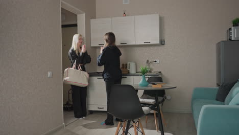 Two young women clap hands together in modern apartment hallway by kitchen, smiling and enjoying playful interaction while greeting each other in cozy indoor friendship moment
