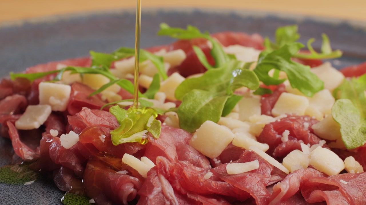 Olio d'oliva versato a filo su carpaccio di manzo fresco con rucola e Parmigiano