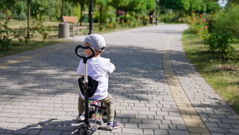 adorable toddler sits on the bike in the park. kid turns around looking at camera. sunny day outdoors.