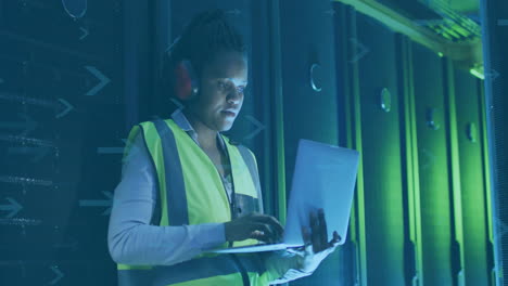 wearing safety vest and headphones, person working on laptop in server room