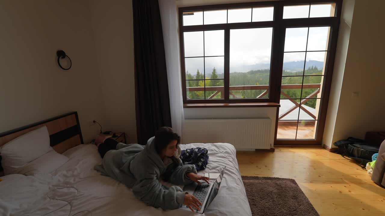 산을 볼 수 있는 호텔 방에서 노트북으로 일하는 여자