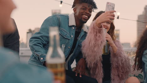 happy multi ethnic friends enjoying weekend rooftop party drinking alcohol taking selfie photos using smartphone sharing on social media