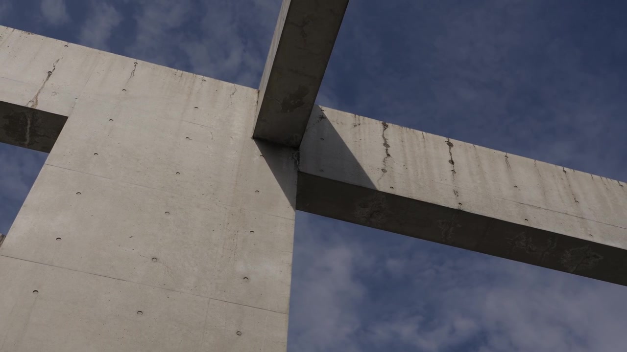Low angle view of weathered concrete structural beams meeting at corner with sky backdrop