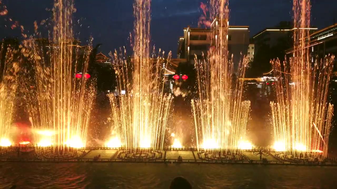 Espetáculo incrível de luzes vermelhas e amarelas e som nas fontes da praça central da cidade ao anoitecer em Xian, China.