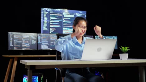 programadora asiática celebrando el éxito escribiendo código en una computadora portátil usando múltiples monitores que muestran la base de datos en terminales ventanas de escritorio en la oficina