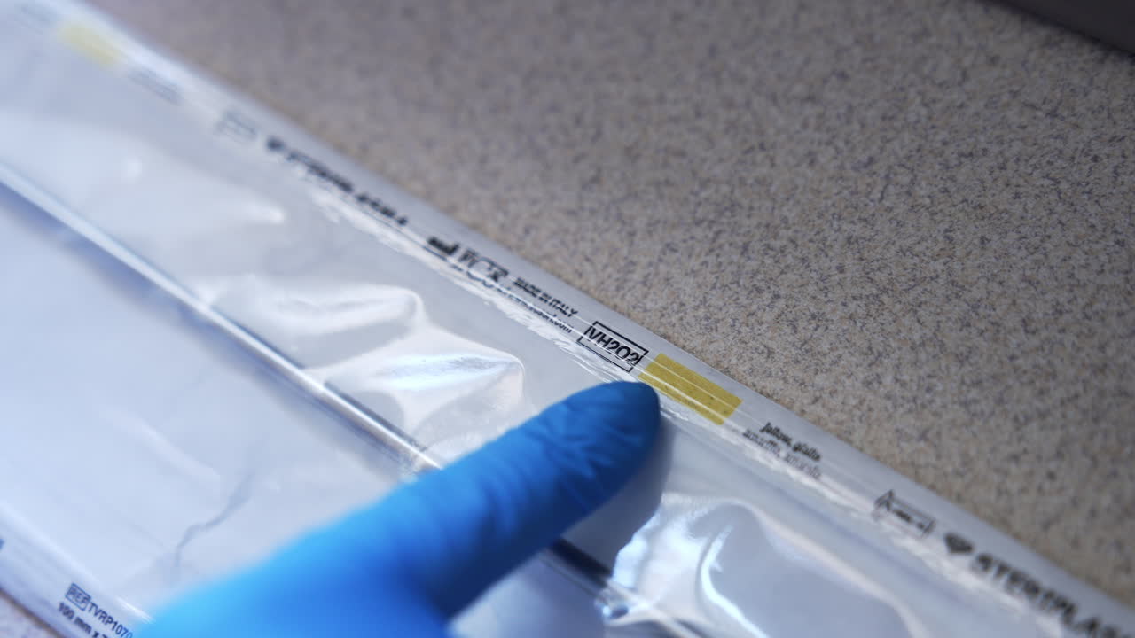 Medic gloved hand touching the plastic bag with metal instrument inside. Close up. Sterilization of tools in equipment. Top view.