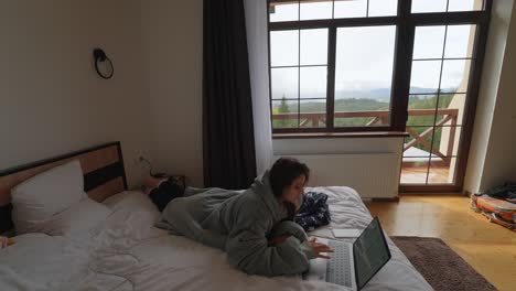 mujer trabajando en una computadora portátil en una habitación de hotel con vista a la montaña